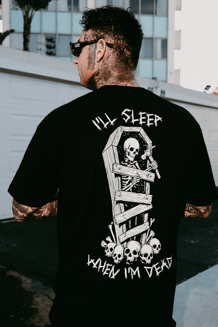 Never Sleepin' graphic tee on model — black t-shirt with skeleton-in-coffin back print, I'll Sleep When I'm Dead